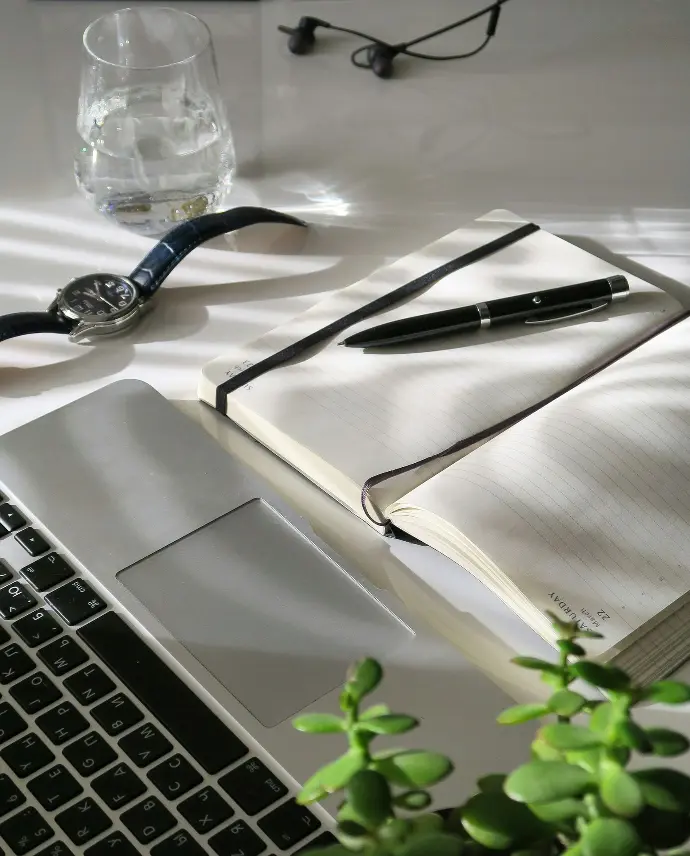 Image qui illustre un besoin de nouvelles compétences avec un ordinateur portable ouvert, un cahier et un stylo à côté, une montre, un verre d'eau, des écouteurs et une plante